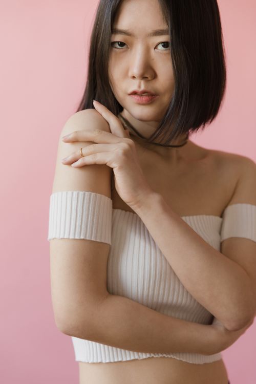 Free Portrait of a young woman in a white off-shoulder top against a pink background. Stock Photo