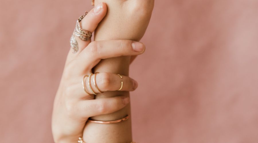 Personne portant un bracelet chaîne doré et plusieurs bagues sur la même main