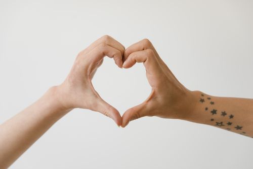 Free Two hands form a heart shape on a white background, one with star tattoos. Stock Photo