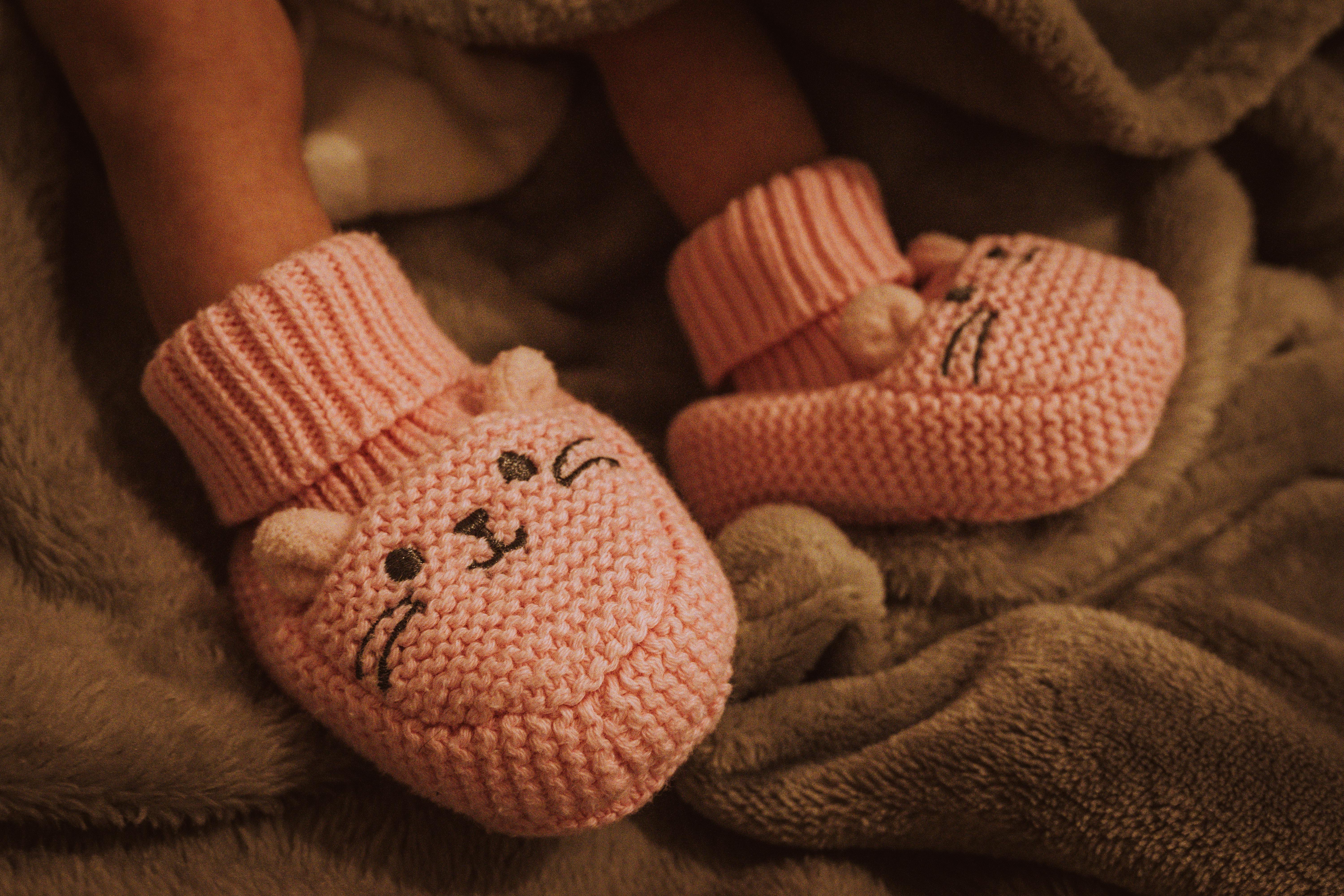Close-up of a baby wearing pink cat-themed knit booties on a soft blanket.