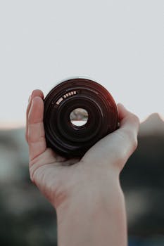 A hand holding a camera lens captures outdoor creativity and photography essence.