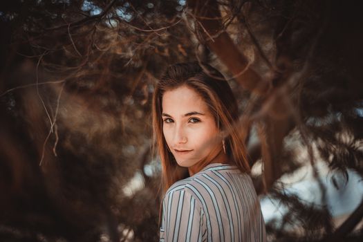A woman in a striped shirt looking over her shoulder among tree branches, creating a moody and artistic portrait.