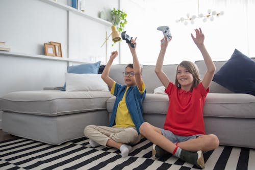 Free A Boy and a Girl Raising Their Hands While Sitting on the Floor Stock Photo