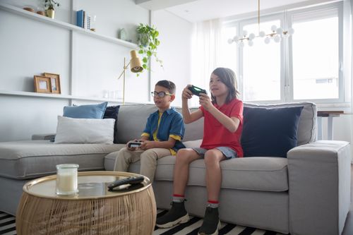 Free Two boys playing video games on a sofa in a modern living room. Bright and fun atmosphere. Stock Photo