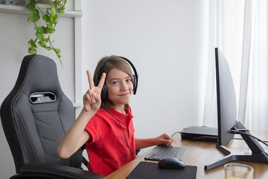 Child in red shirt making peace sign while gaming indoors with computer setup.