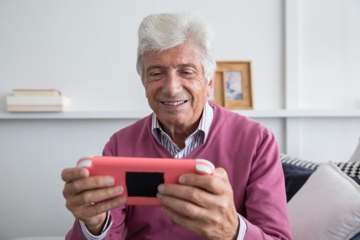 Elderly man smiling while playing on a handheld console indoors.
