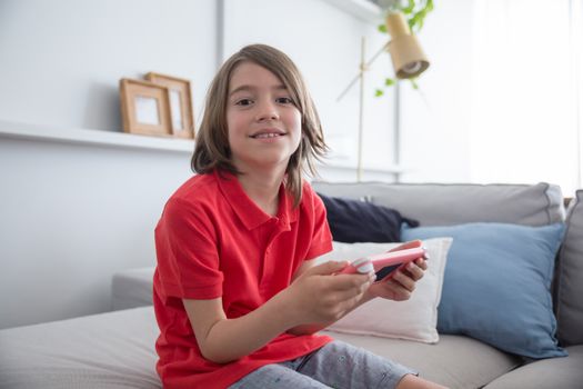 Young boy smiling while playing video games indoors on a couch.