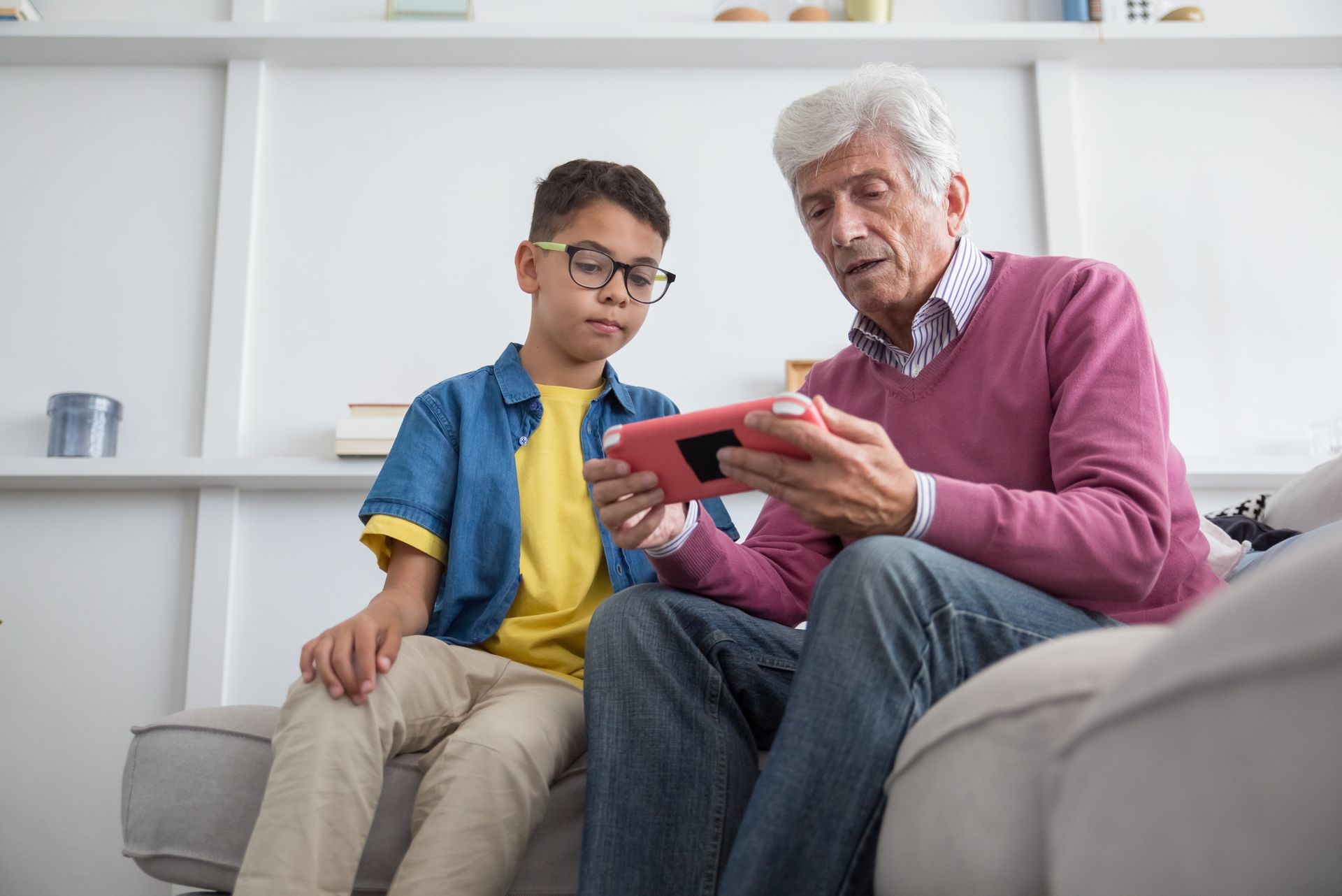 Elderly man and boy sharing a moment with a tablet on the sofa.