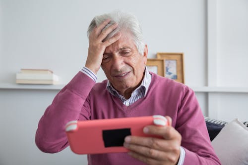 An Elderly Man Holding his Forehead While Holding the Pink Nintendo Switch