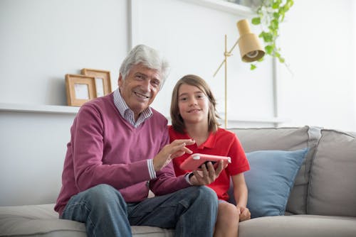 An Elderly Man with His Granddaugther Smiling while Sitting on the Couch