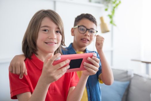 Two boys happily playing with a tablet indoors, embracing and smiling. Technology and friendship concept.