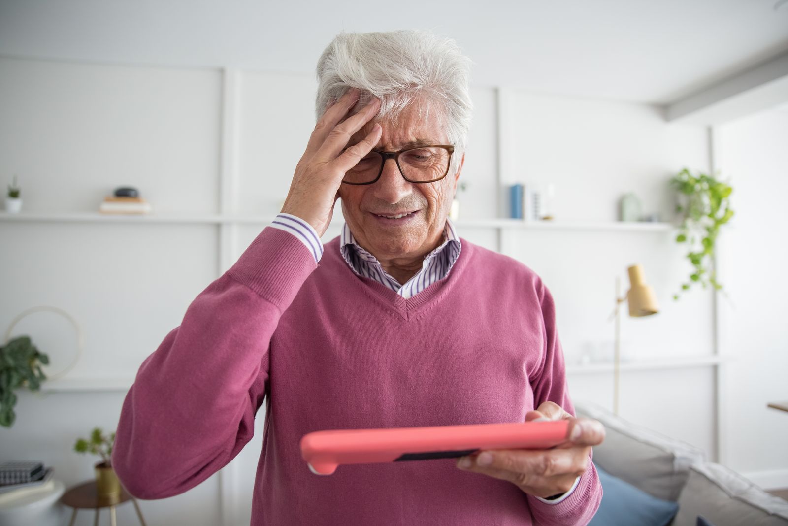 An older man with one hand on his forehead, looking at a tablet