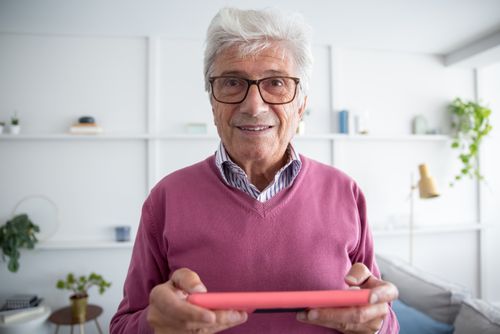 Free Senior man in purple sweater using a tablet indoors, smiling and engaged. Stock Photo