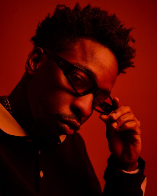 Stylish African American man with eyeglasses posing confidently in dramatic red lighting.