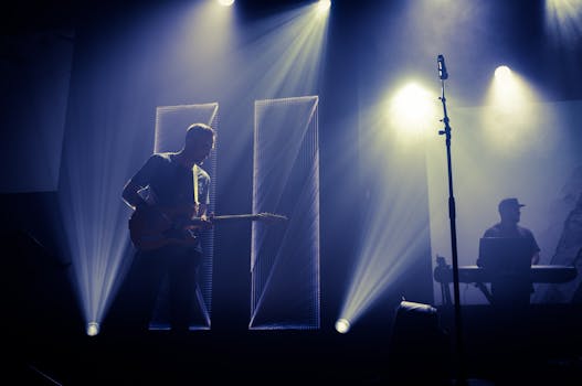 In a dimly lit club, a guitarist and keyboardist perform live on stage, surrounded by dramatic lights and shadows.