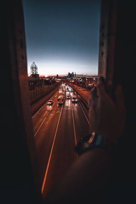 A view of busy highway traffic with a distant city skyline at dusk, framed by a structure.