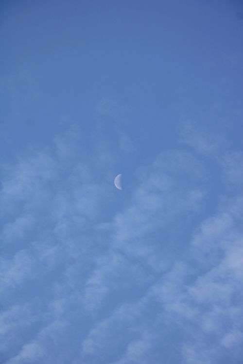 Free A serene view of a crescent moon surrounded by wispy clouds against a blue sky. Stock Photo
