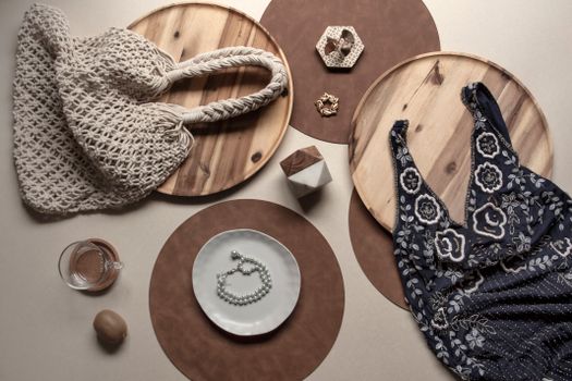 Flat lay of bohemian style accessories and attire including a bag, dress, and jewelry on rustic wooden surfaces.