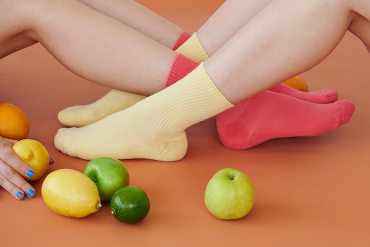 Close-up Of Women Feet In Colorful Socks Sitting With Fruit Scattered Around 