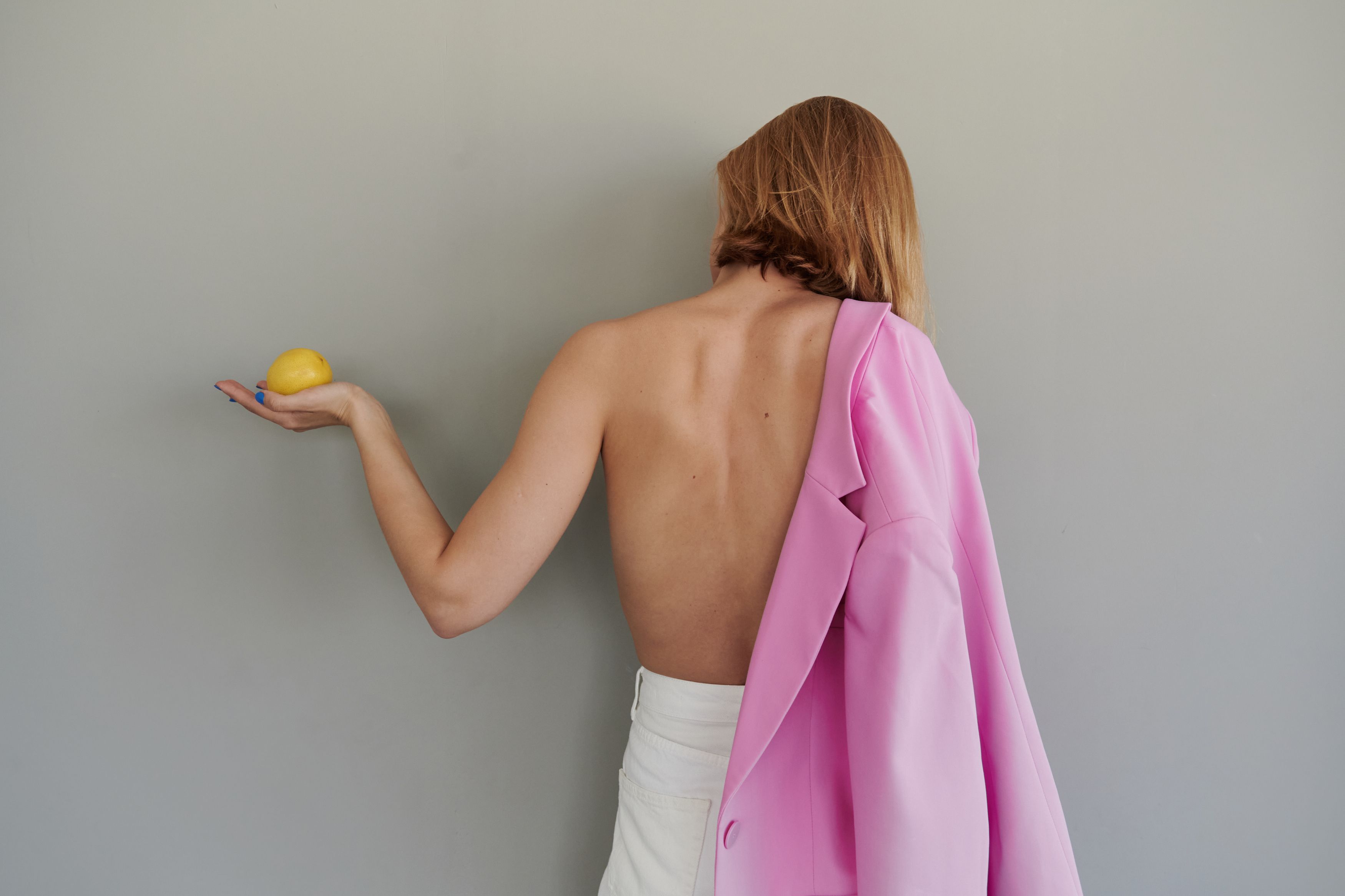 A hand gently pinching the shoulder area of a women's blazer on a hanger, demonstrating where to begin the in-store construction inspection.