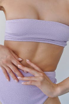 Close-up of a woman's midsection in lilac swimwear, highlighting smooth skin and elegant hand posture.
