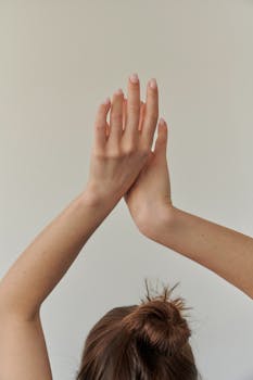 Elegant portrait of a woman's hands raised gracefully against a simple background.