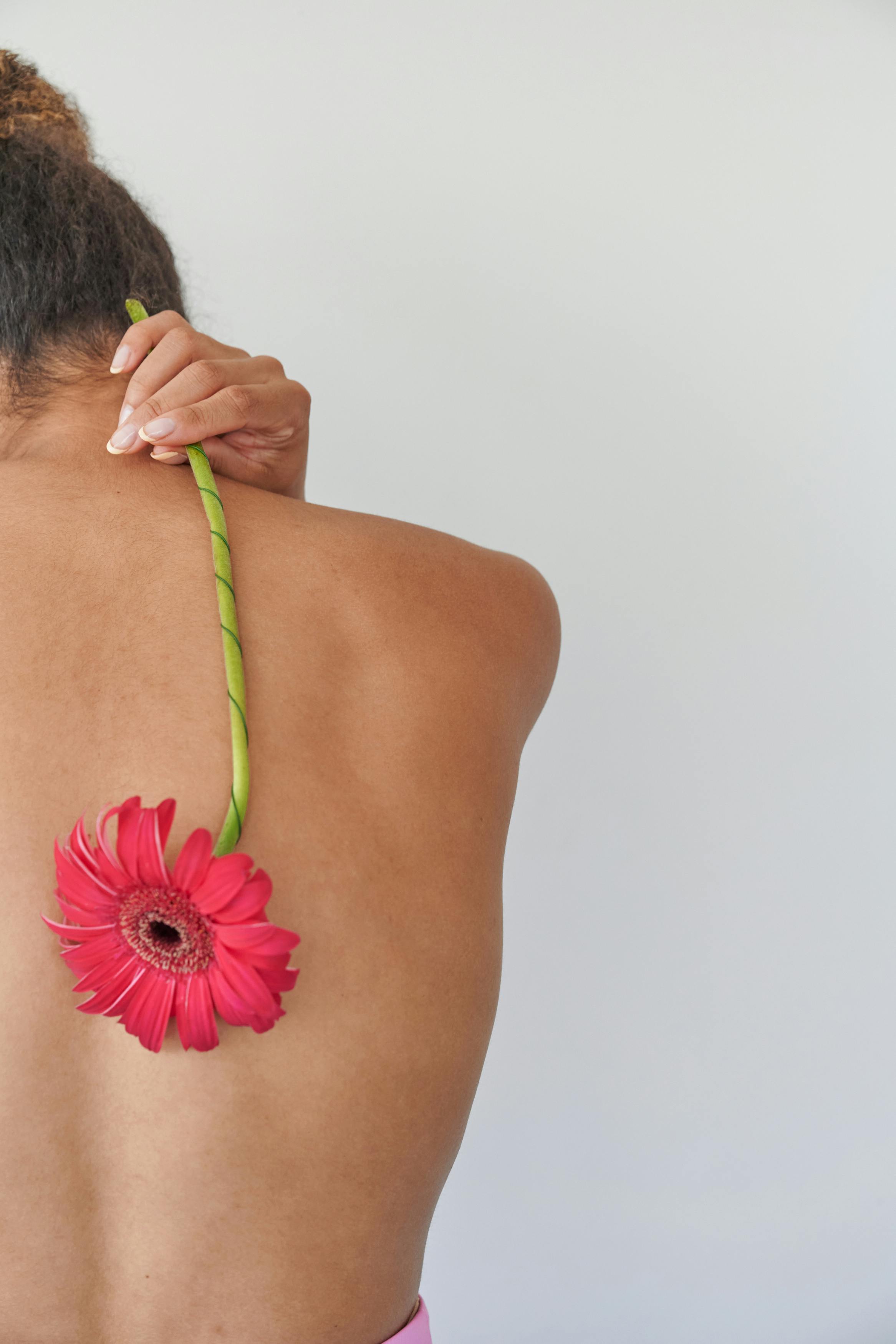 back view naked woman holding pink gerbera flower