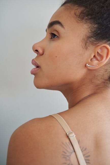 Artistic side profile of a woman with an earring and tattoo, gazing upward.