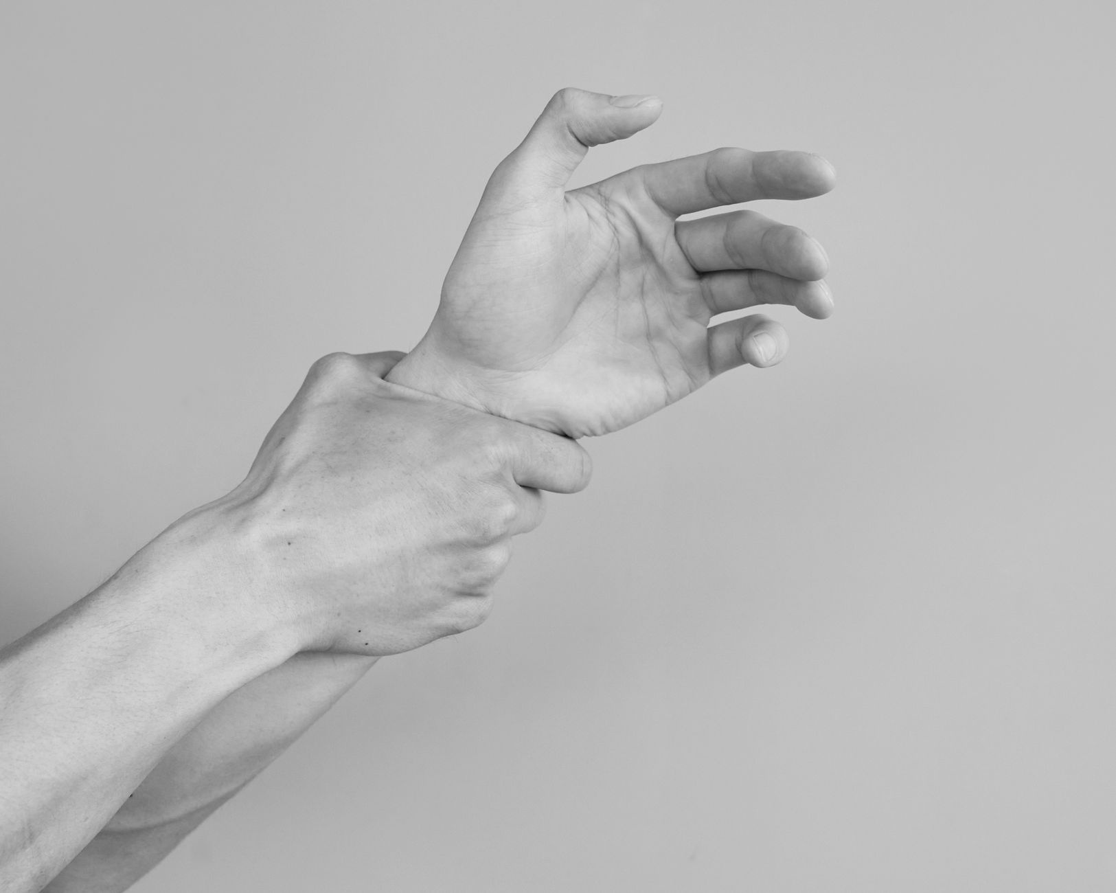 Grayscale image of hands gripping a wrist, symbolizing tension or support.