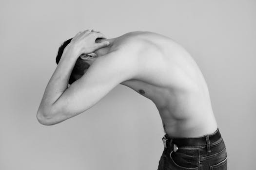 Black and white image of a shirtless man bending in a studio. Artistic and modern composition.