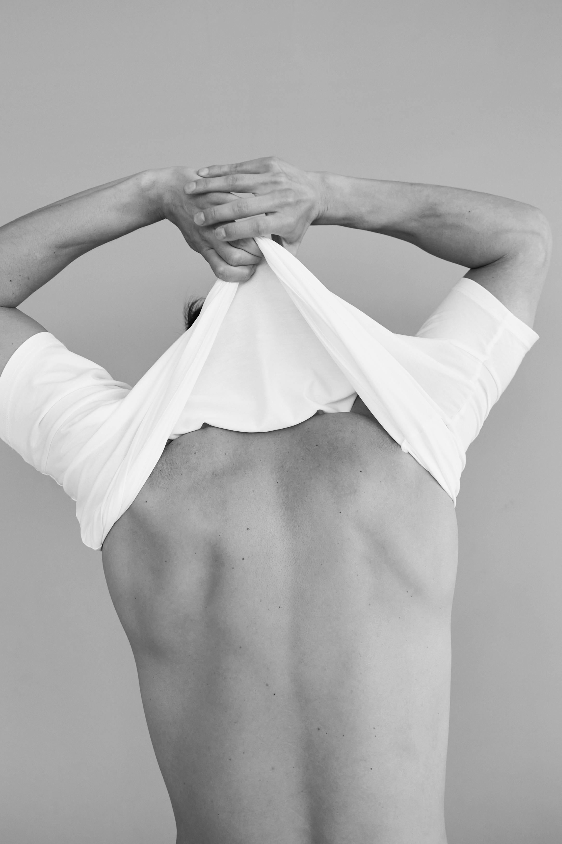 Artistic black and white photo of a man in back view removing his shirt.