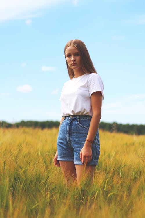 Femme Portant Un T Shirt à Col Rond Blanc, Short Court à Manchette En Denim Bleu En Se Tenant Debout Sur Le Terrain En Herbe