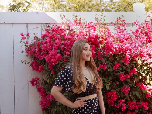 Free Young woman in polka dot dress smiling by vibrant pink blossoms. Stock Photo