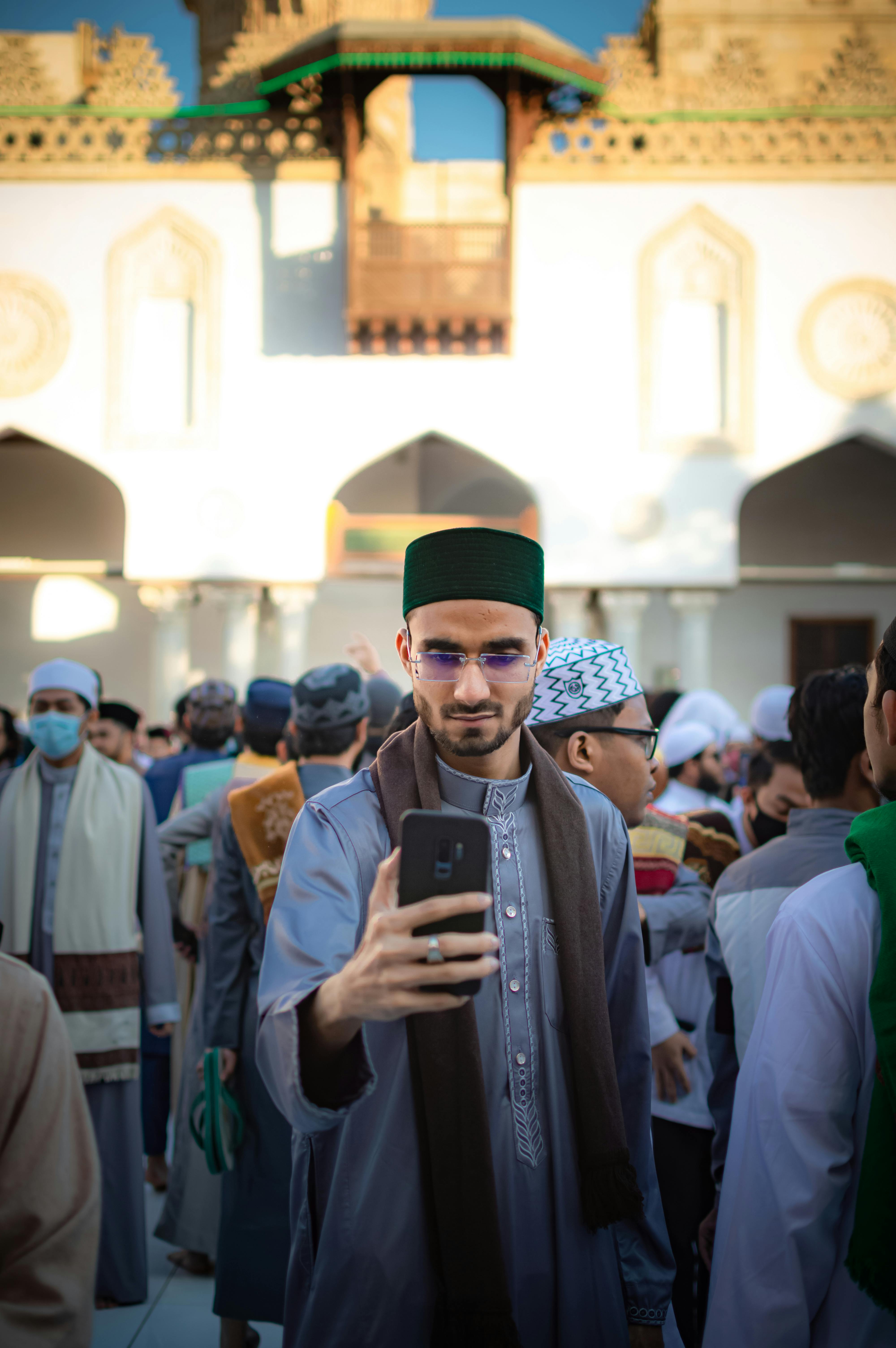 arabic man standing in a crowd in front of a mosque and using his phone