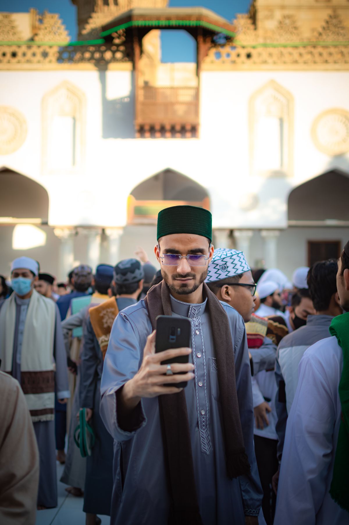 Arabic man standing in a crowd in front of a mosque using his phone