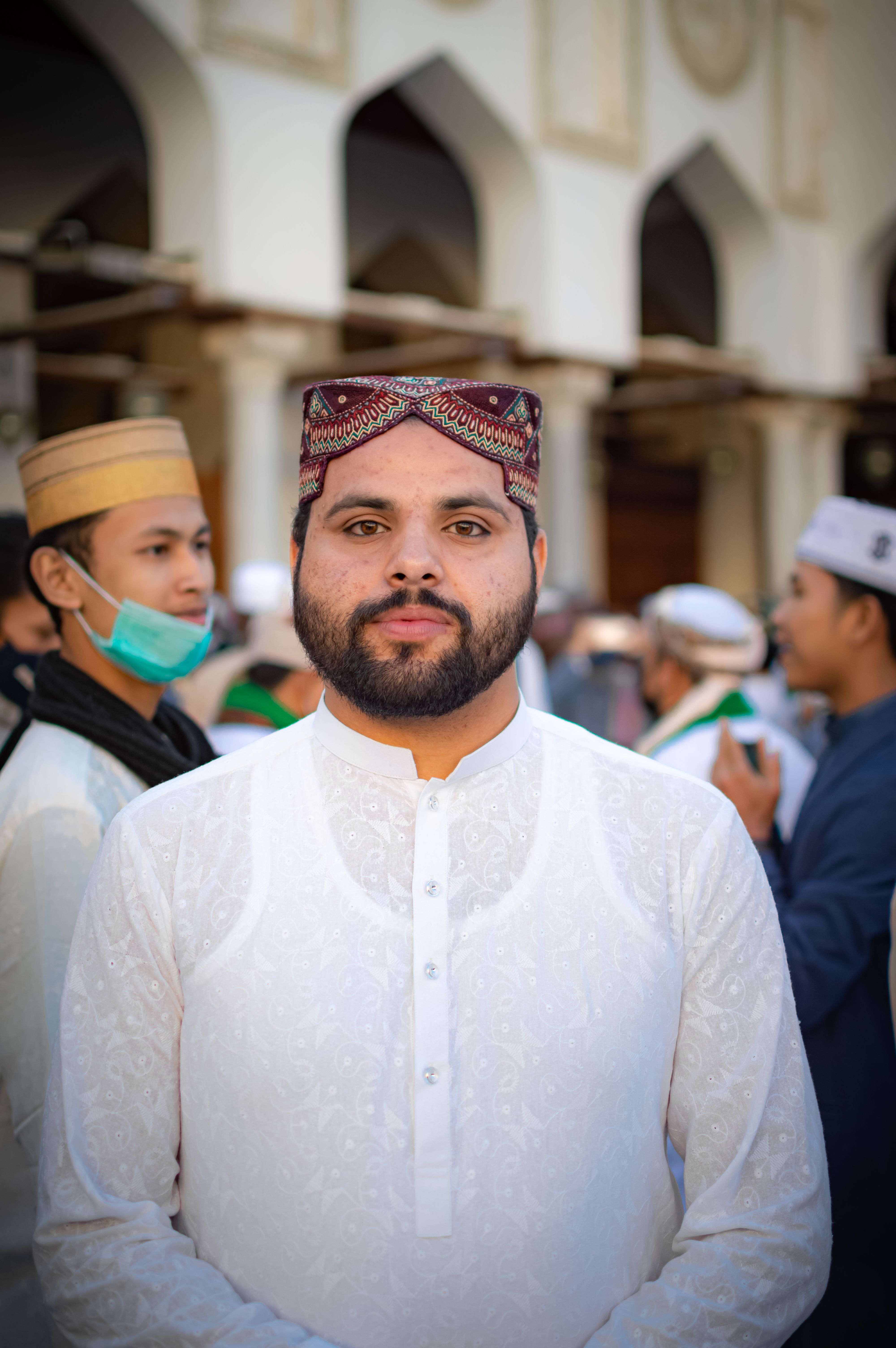A bearded man in traditional clothing standing outdoors during the day.