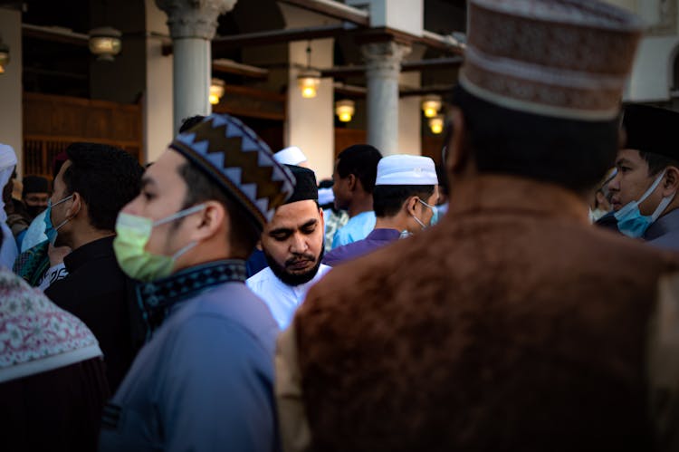 Men In A Crowd Wearing Rounded Caps And Facemasks