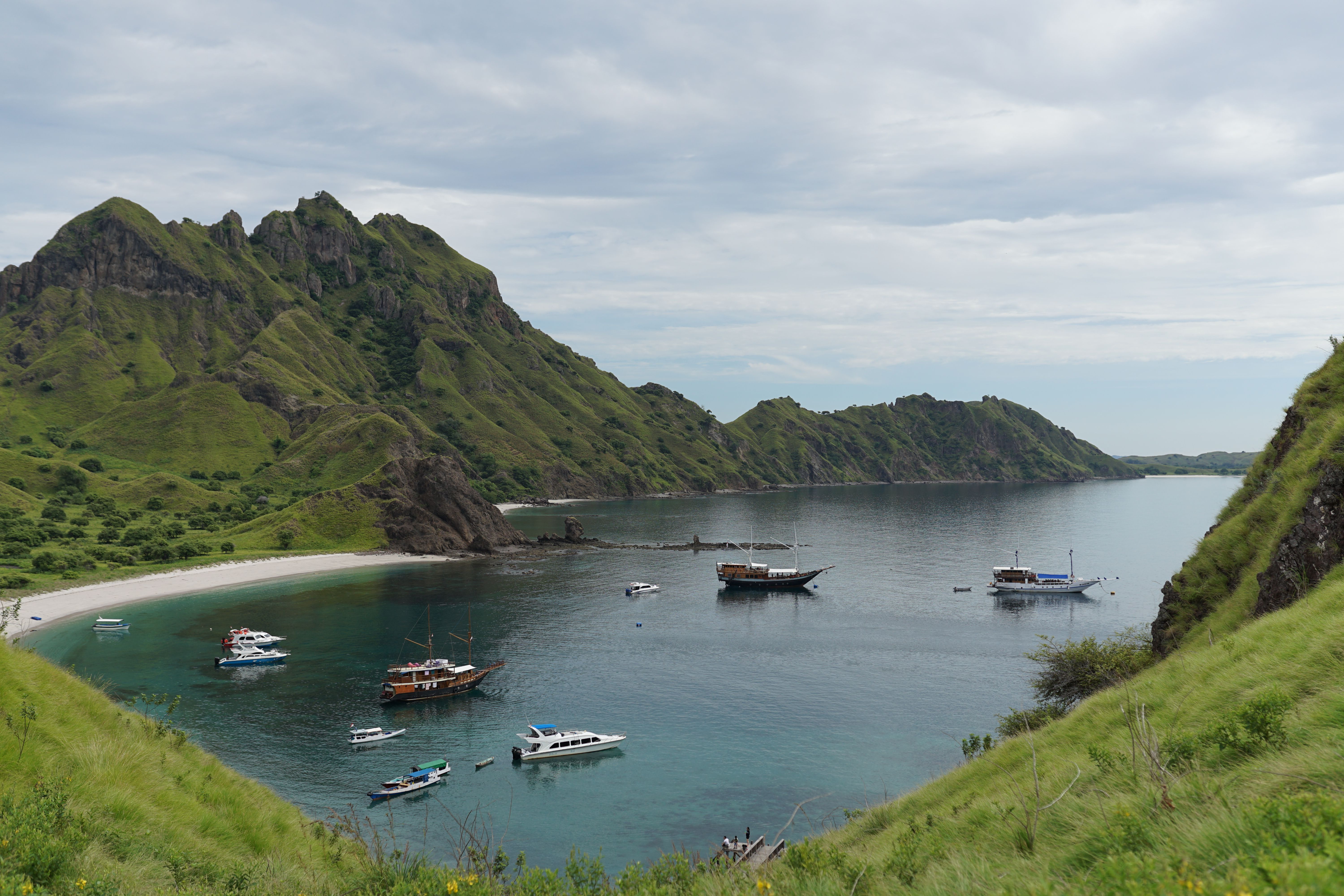 Small wooden boat anchored in a turquoise bay backed by low scrubby headlands