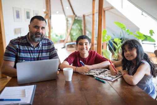 A Man Using a Laptop beside his Kids on a Table