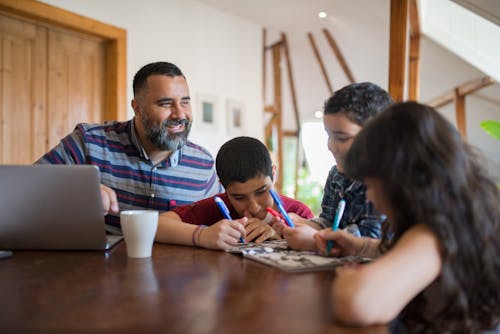 A Man Using a Laptop beside his Kids on a Table