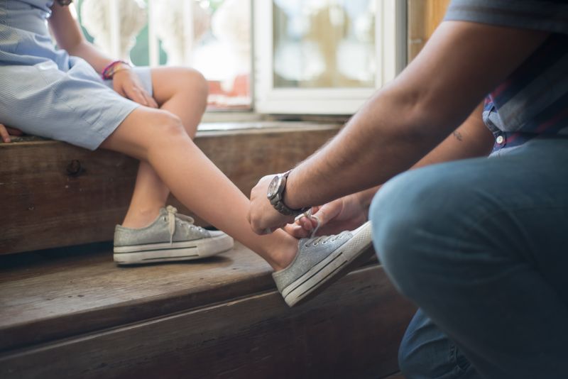 An adult helping a child tie shoelaces indoors