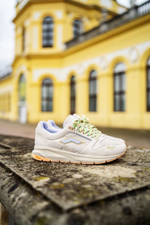 Free A stylish white sneaker on a textured surface with a historical building in the background. Stock Photo