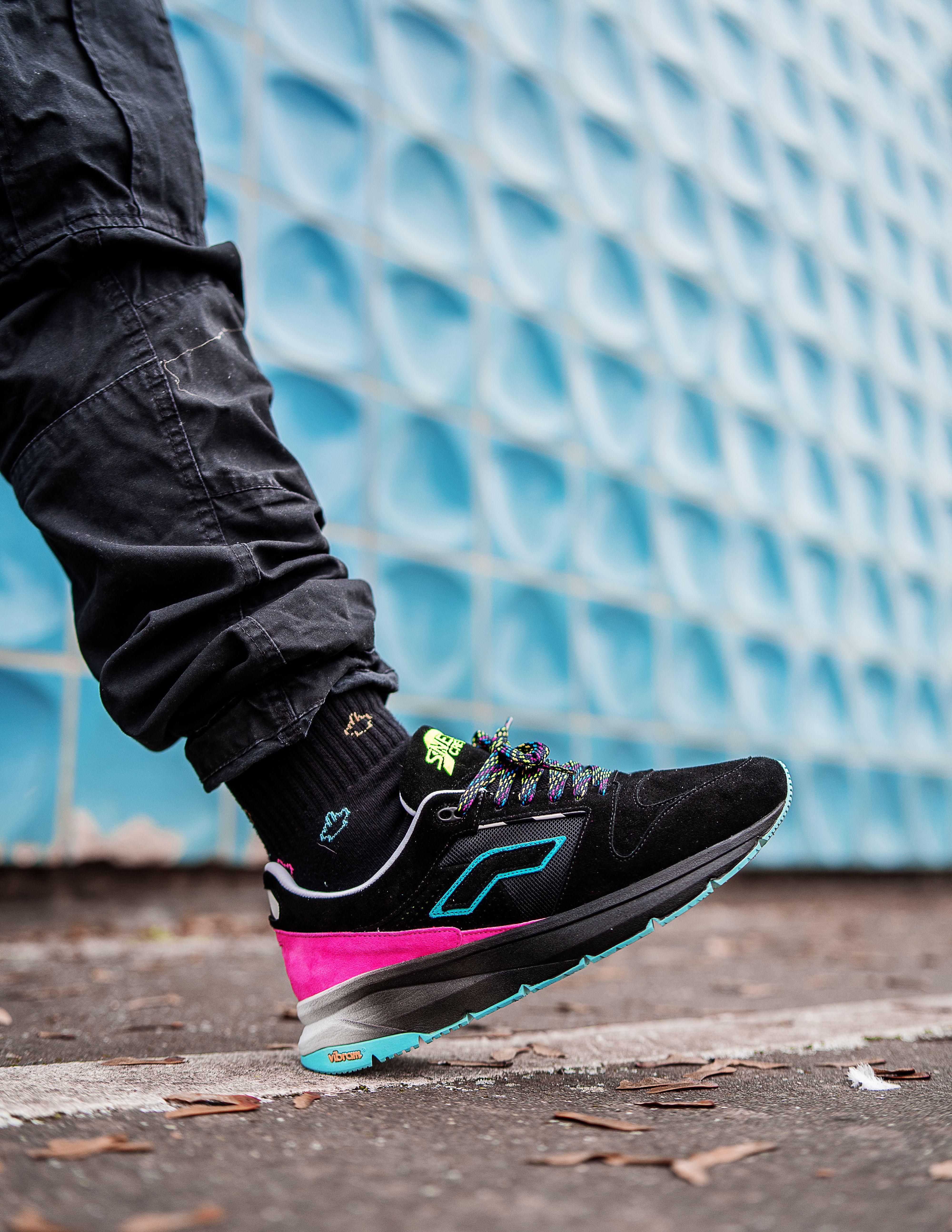 Close-up of a stylish sneaker on urban pavement against textured blue wall.