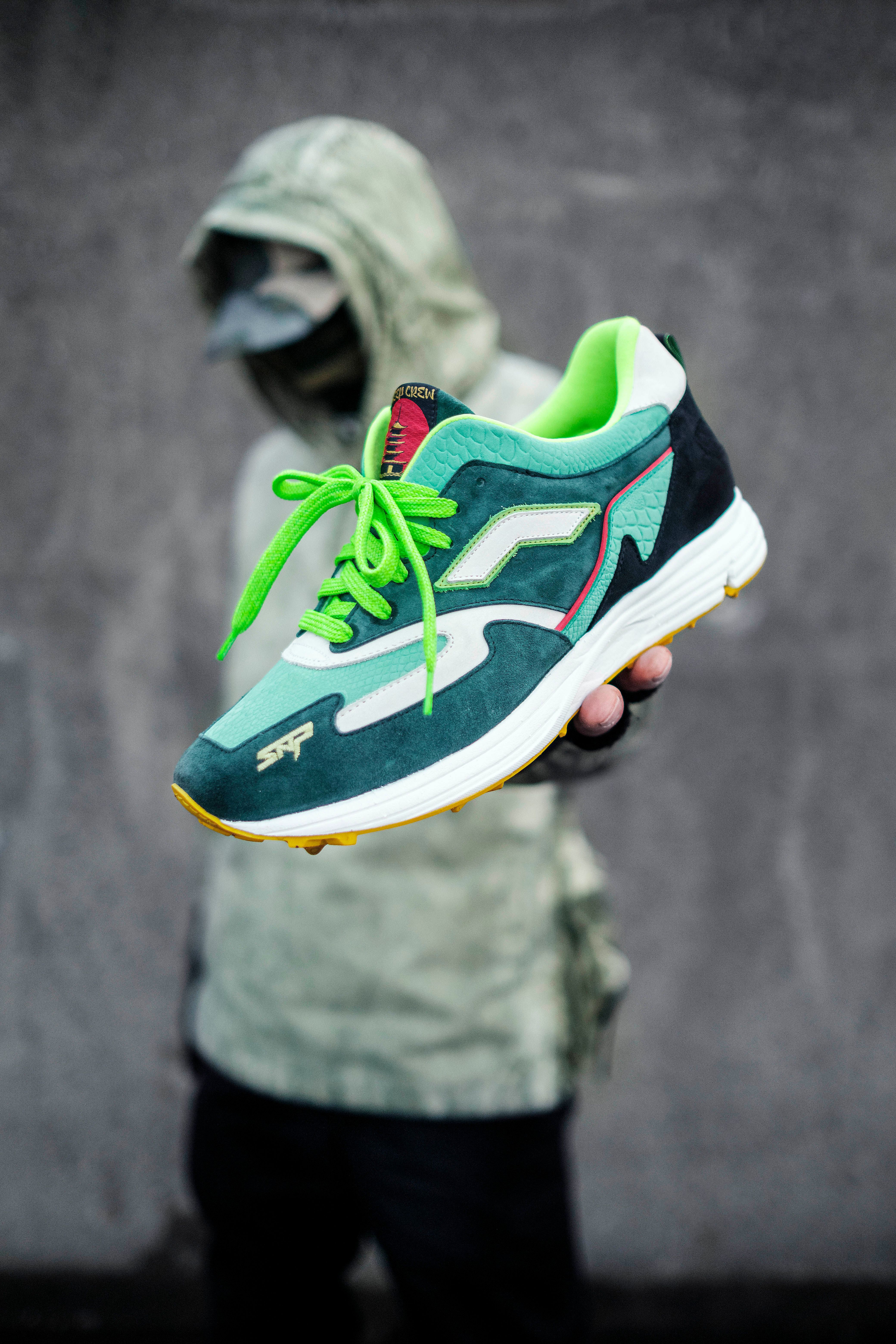 Close-up of stylish green sneakers held by a person in a hoodie.