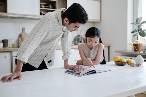 Free Father and daughter bonding over a cookbook in a modern kitchen setting. Stock Photo