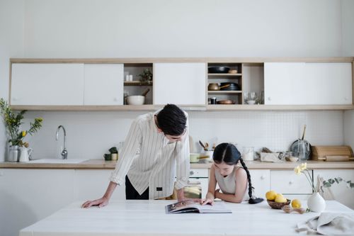 Free A father and daughter explore a cookbook together in a sleek, minimalist kitchen setting. Stock Photo