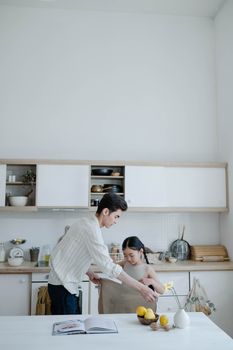 Father and daughter bonding in kitchen, preparing food with white decor.