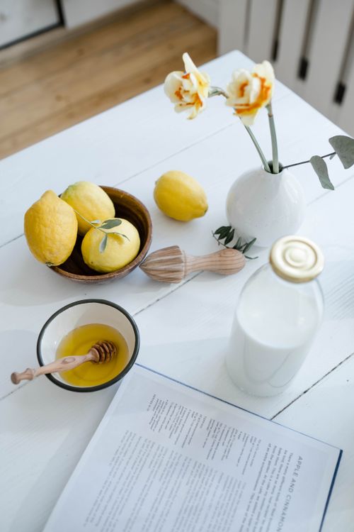 Free Aesthetic arrangement of lemons, honey, and milk on a white table with flowers. Stock Photo