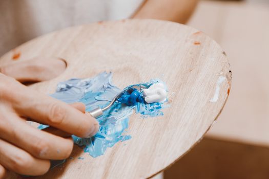 Close-up of artist's hand mixing blue and white paint on a wooden palette.