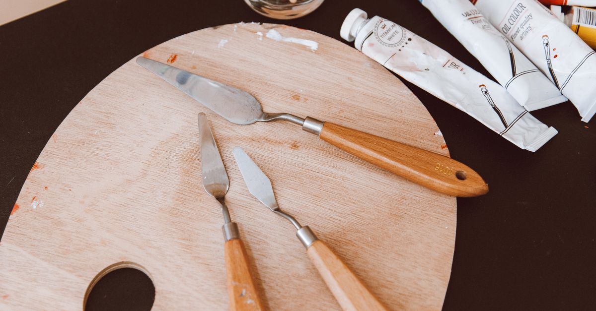 Close-up of an artist's palette with painting tools and tubes of paint, set in a studio.